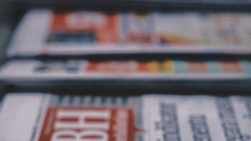 A stacked pile of printed newspapers showing front-page headlines.